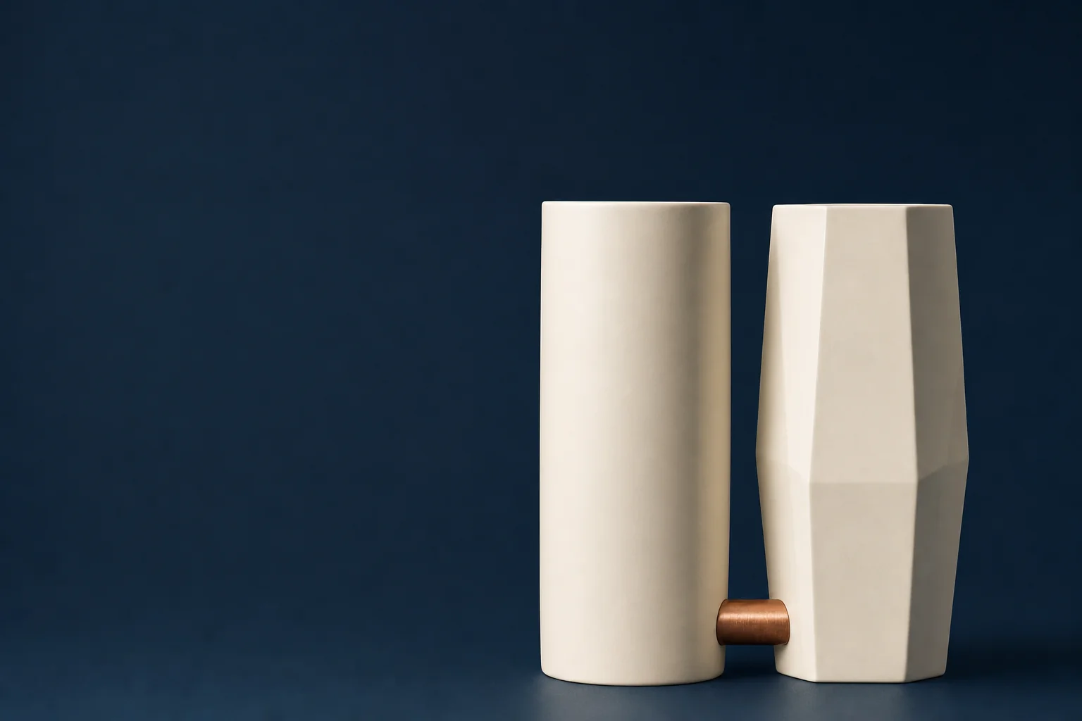 Two plain ivory forms of equal height on a navy background, one smooth and one faceted, joined near the base by a short copper bar