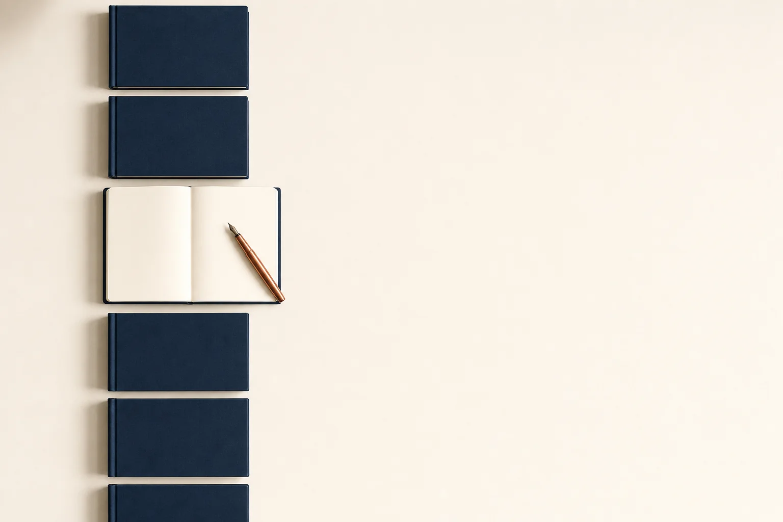 A row of identical navy notebooks on a desk with one open to a blank page and a copper pen resting across it