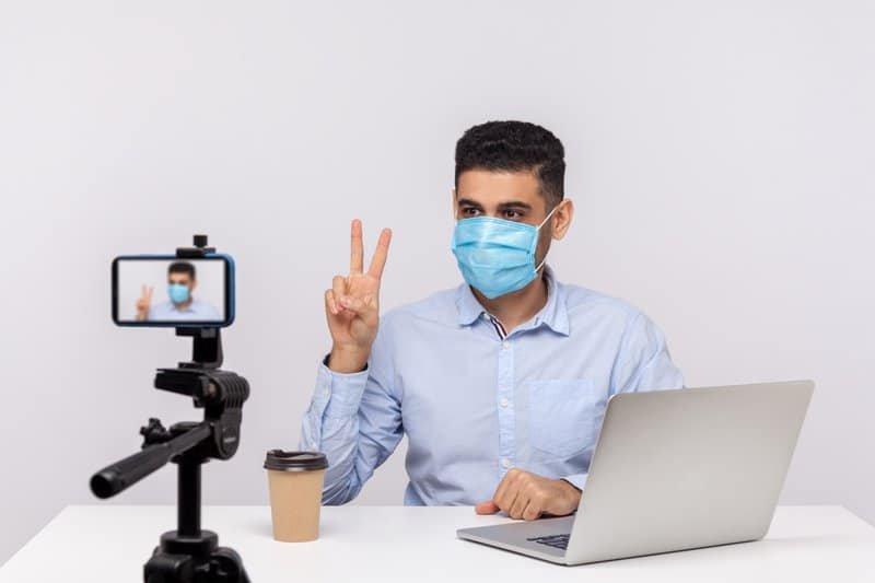 Man in hygienic mask gesturing victory making video about recovery after flu, coronavirus infection, giving tips on using protect filter against contagious disease. studio shot, white background